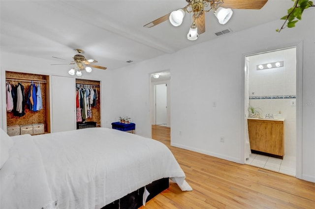 bedroom featuring ensuite bathroom, multiple closets, visible vents, light wood finished floors, and baseboards