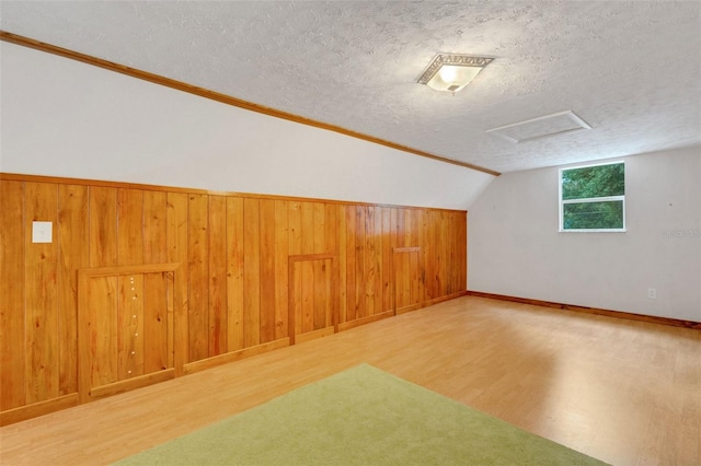 bonus room with lofted ceiling, a textured ceiling, baseboards, wood walls, and wood finished floors