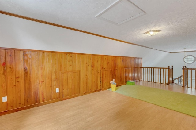 additional living space with wood walls, lofted ceiling, a textured ceiling, and wood finished floors