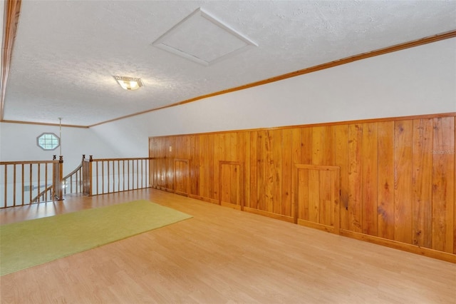 additional living space with wooden walls, a textured ceiling, and wood finished floors