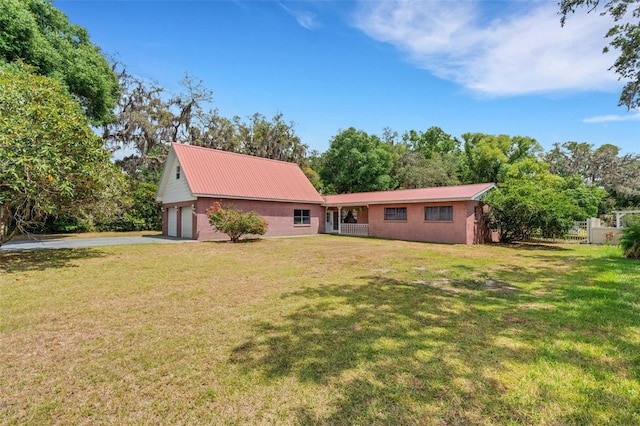 back of house featuring a lawn, driveway, and metal roof