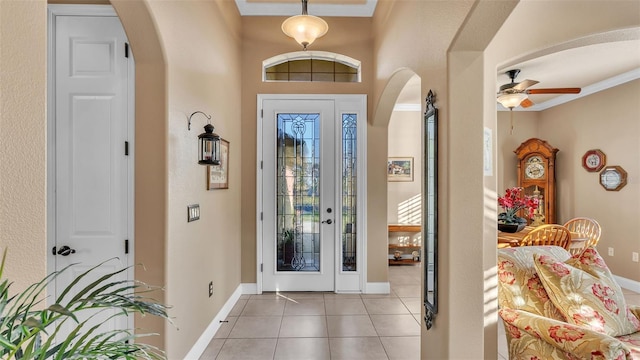 entryway with arched walkways, ceiling fan, light tile patterned flooring, baseboards, and crown molding