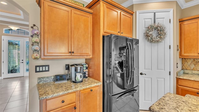 kitchen with black refrigerator with ice dispenser, ornamental molding, tasteful backsplash, light stone countertops, and light tile patterned floors