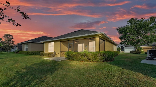back of property at dusk with a lawn, stucco siding, and a ceiling fan