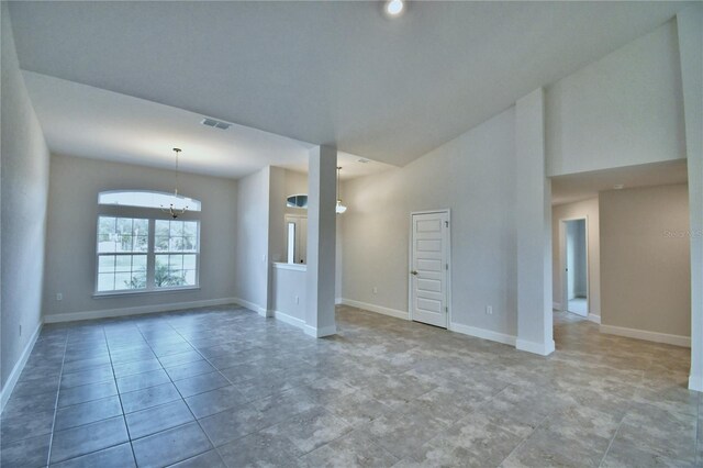 empty room featuring a chandelier, baseboards, and a high ceiling