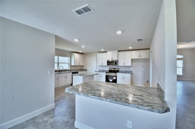 kitchen with stainless steel appliances, a textured wall, light tile patterned flooring, a sink, and baseboards