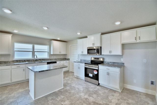 kitchen featuring stainless steel appliances, a sink, light stone countertops, white cabinets, and a center island