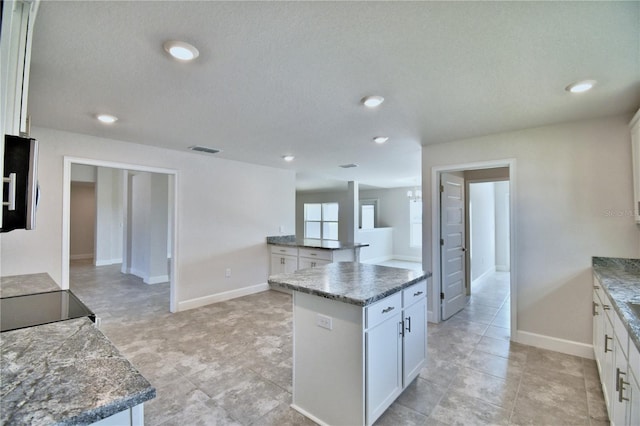 kitchen featuring white cabinets, a kitchen island, baseboards, a textured ceiling, and stone counters