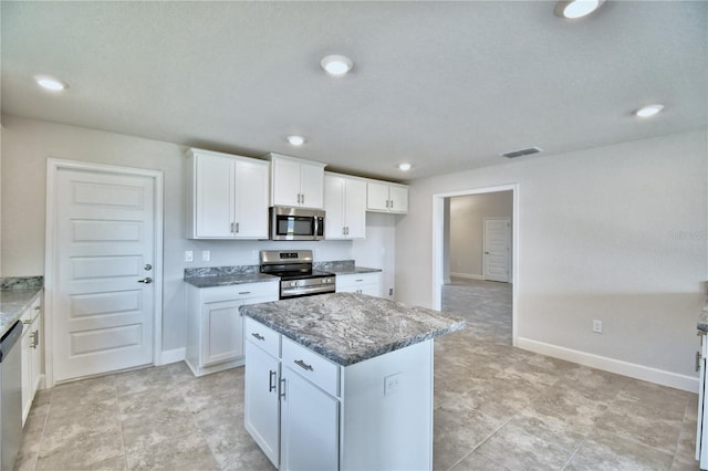 kitchen with stainless steel appliances, dark stone counters, white cabinetry, a kitchen island, and baseboards