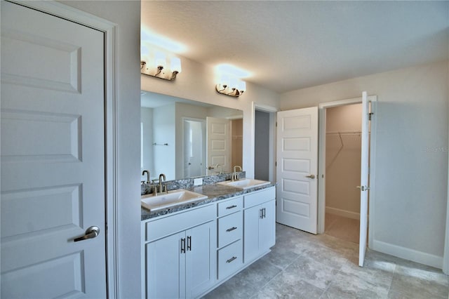 full bath featuring double vanity, a walk in closet, and baseboards