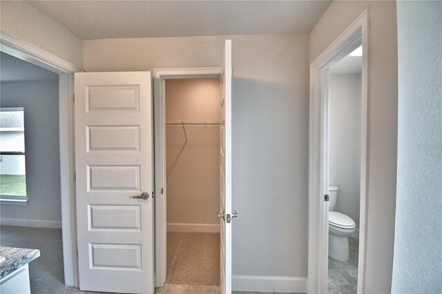 bathroom featuring toilet, vanity, baseboards, and a walk in closet