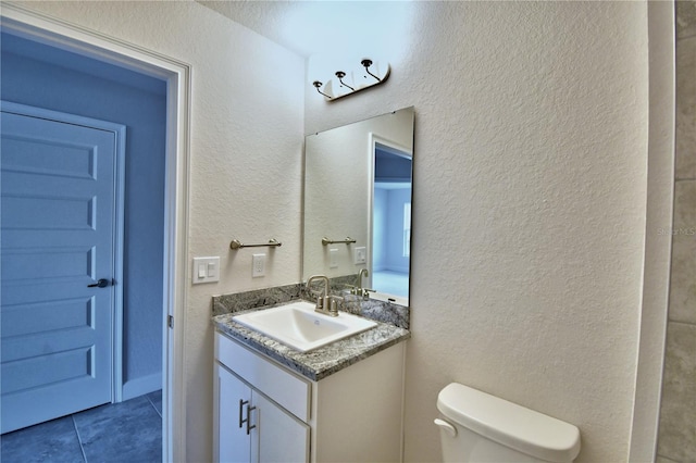 bathroom with tile patterned flooring, toilet, vanity, and a textured wall