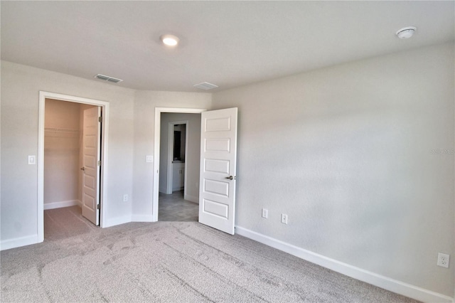 unfurnished bedroom with light colored carpet, a walk in closet, baseboards, and a closet