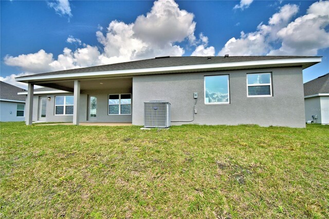 rear view of property with stucco siding, cooling unit, a lawn, and a patio