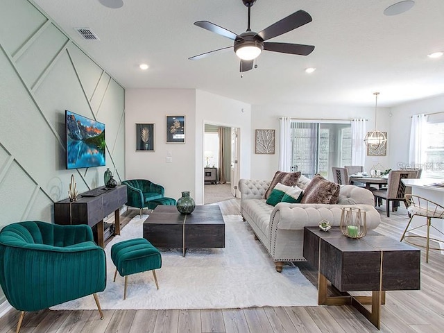 living room with light wood-style floors, visible vents, ceiling fan with notable chandelier, and recessed lighting