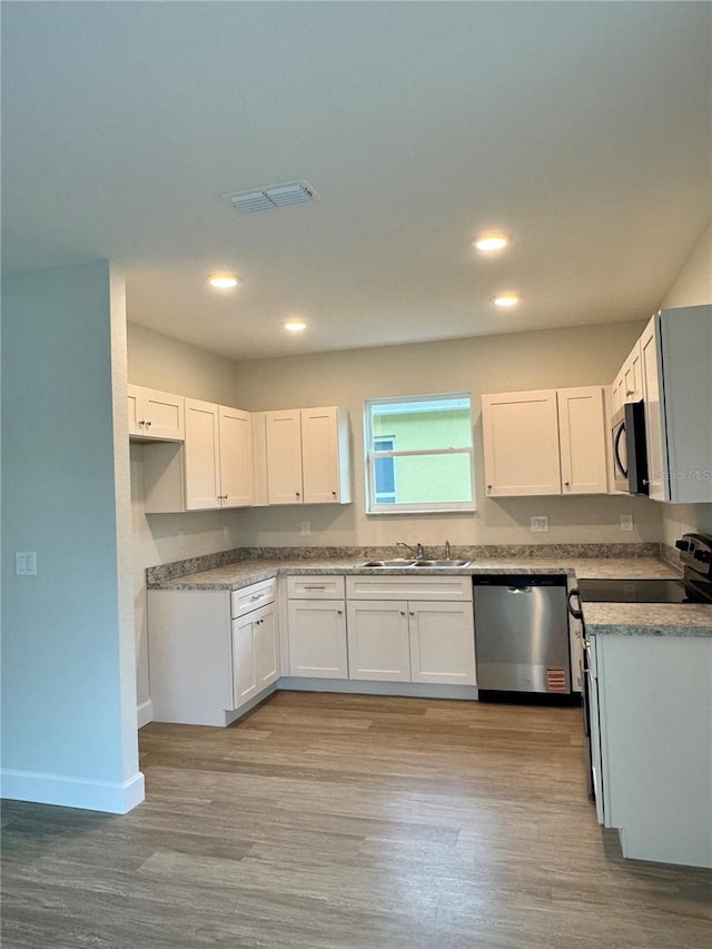 629 W 9th, Lakeland, FL 33805 - kitchen with stainless steel dishwasher, a sink, light wood finished floors, white cabinetry, and baseboards
