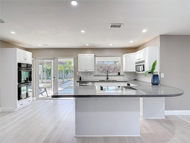 kitchen featuring a sink, white cabinetry, visible vents, black appliances, and light wood-style floors