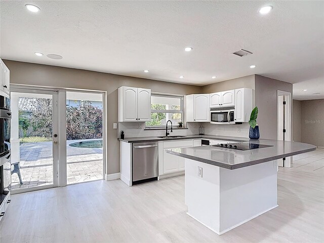 kitchen with a sink, light wood-style flooring, white cabinets, dark countertops, and appliances with stainless steel finishes