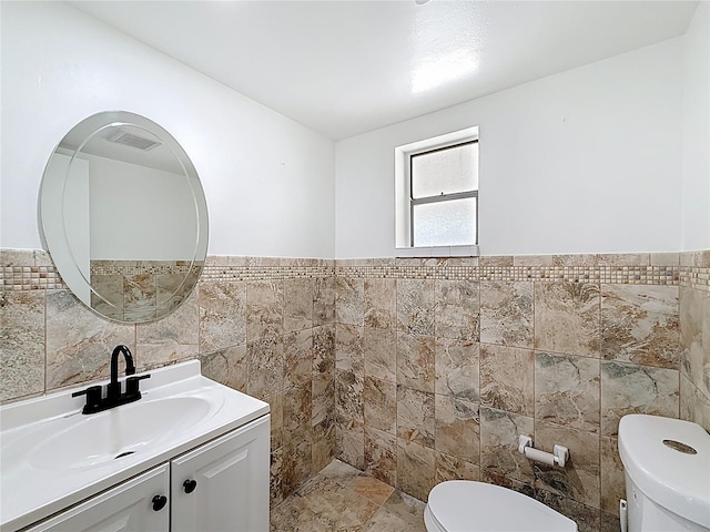 half bath with a wainscoted wall, vanity, tile walls, and toilet