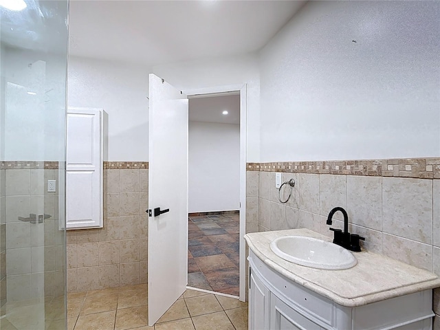 full bath featuring tile walls, vanity, a wainscoted wall, and tiled shower