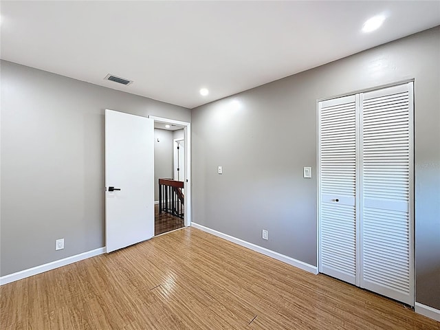 unfurnished bedroom featuring wood finished floors, a closet, visible vents, baseboards, and recessed lighting