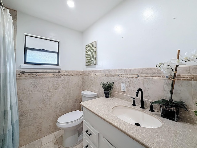 bathroom featuring toilet, tile walls, vanity, tile patterned floors, and wainscoting