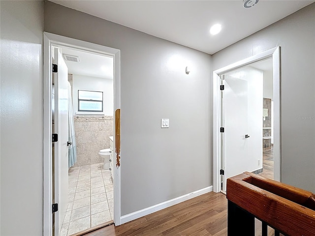 hall featuring light wood finished floors, baseboards, and visible vents