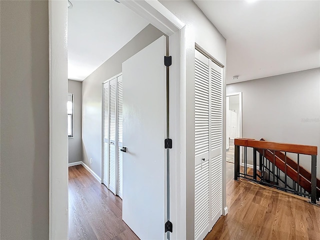 corridor featuring wood finished floors, an upstairs landing, and baseboards