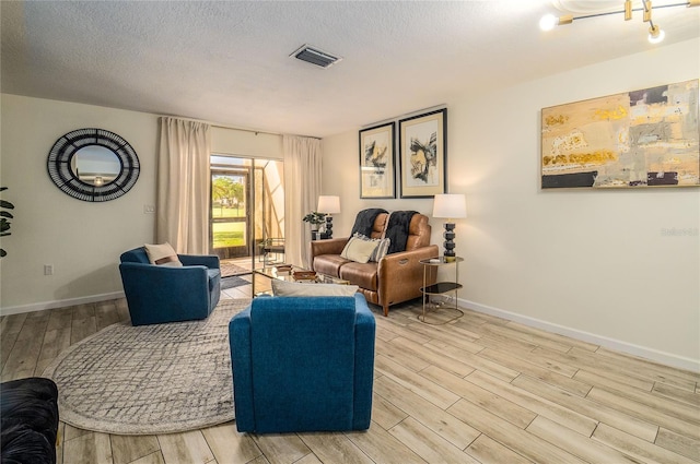 living area with light wood-type flooring, baseboards, and a textured ceiling
