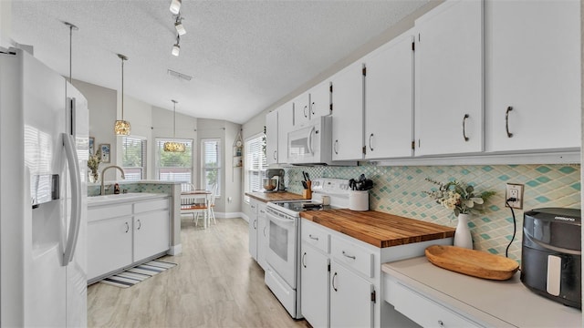 kitchen with white appliances, a textured ceiling, vaulted ceiling, a sink, and white cabinets