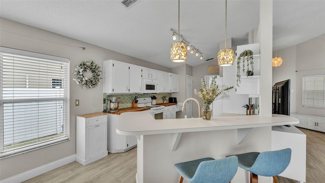 kitchen with white appliances, light wood finished floors, a kitchen bar, plenty of natural light, and vaulted ceiling