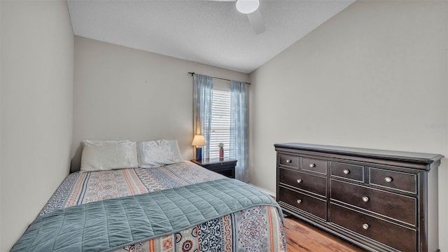 bedroom with light wood finished floors, vaulted ceiling, a ceiling fan, and a textured ceiling