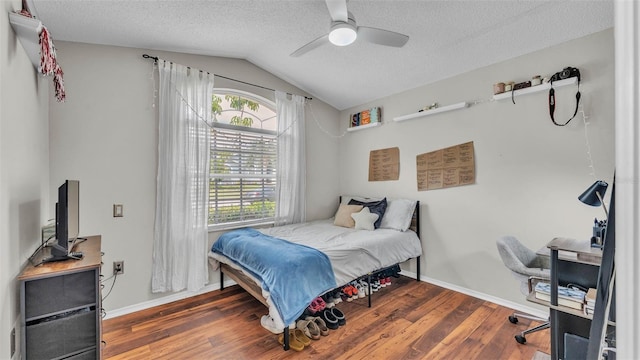 bedroom featuring vaulted ceiling, wood finished floors, a textured ceiling, baseboards, and a desk