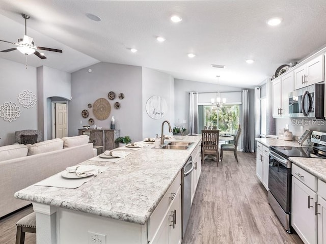 kitchen with wood finished floors, a sink, stainless steel appliances, a center island with sink, and vaulted ceiling