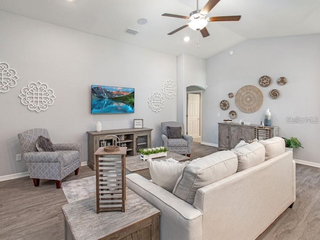 living room with lofted ceiling, baseboards, visible vents, ceiling fan, and wood finished floors