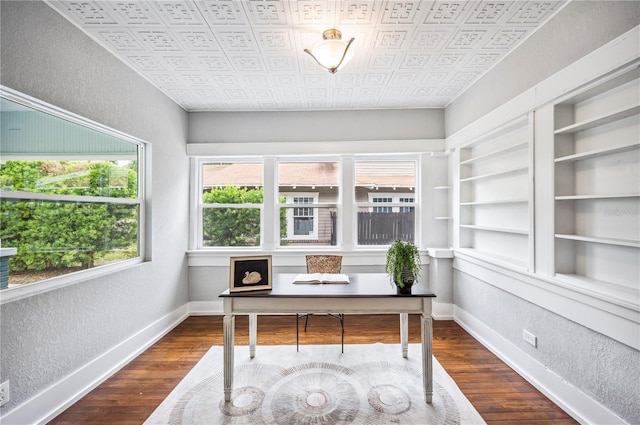office featuring a textured wall, dark wood finished floors, baseboards, and an ornate ceiling