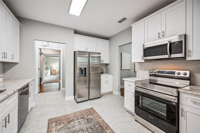 kitchen with stainless steel appliances, backsplash, white cabinets, baseboards, and light stone countertops