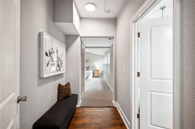 corridor with dark wood-style flooring, a textured wall, and baseboards