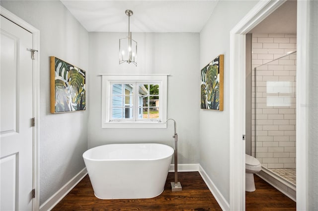 full bath featuring baseboards, a stall shower, a chandelier, wood finished floors, and a soaking tub