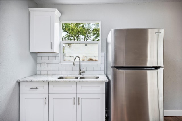 kitchen with freestanding refrigerator, a sink, decorative backsplash, and white cabinetry