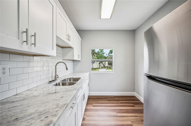 kitchen featuring freestanding refrigerator, a sink, baseboards, tasteful backsplash, and wood finished floors
