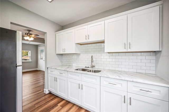 kitchen with freestanding refrigerator, a sink, wood finished floors, white cabinetry, and tasteful backsplash