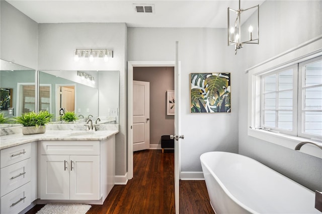 bathroom featuring wood finished floors, vanity, a freestanding tub, a chandelier, and baseboards