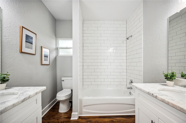 full bathroom featuring wood finished floors, two vanities, shower / bathtub combination, toilet, and a textured wall