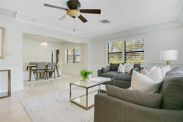 living room with baseboards, ornamental molding, attic access, and a ceiling fan