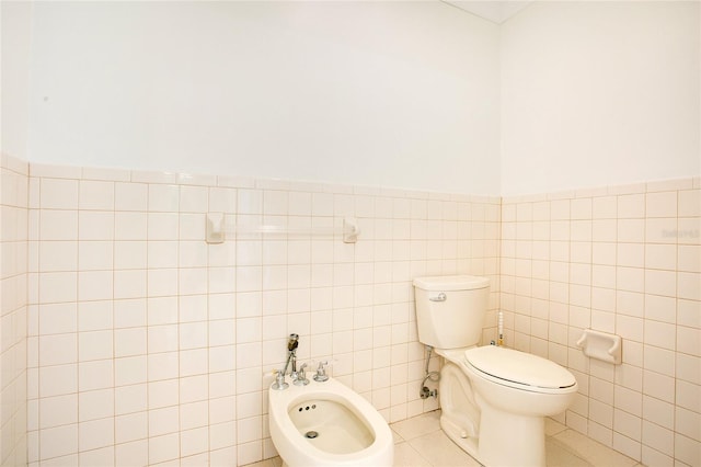 bathroom with tile walls, toilet, a bidet, and tile patterned floors
