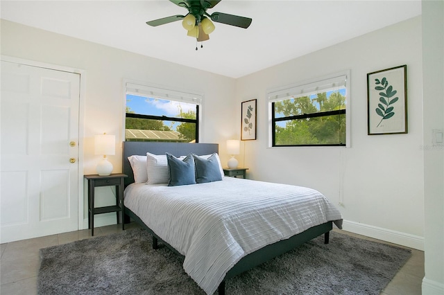 tiled bedroom with multiple windows, a ceiling fan, and baseboards