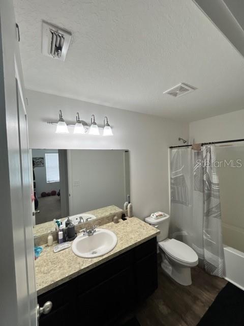 879 Grandin St, Davenport, FL 33837 - bathroom with wood finished floors, toilet, shower / tub combo, vanity, and a textured ceiling