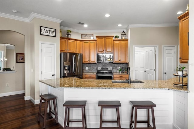8909 N Campbell Rd, Lakeland, FL 33810 - kitchen featuring appliances with stainless steel finishes, a peninsula, a breakfast bar, light stone countertops, and dark wood-type flooring