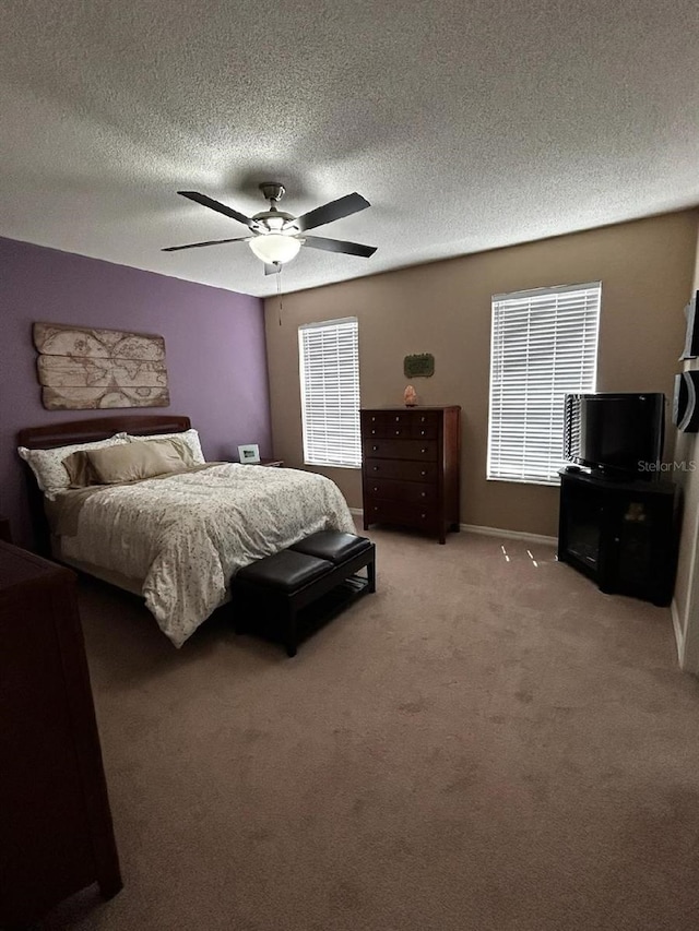bedroom featuring a textured ceiling, light carpet, ceiling fan, multiple windows, and baseboards